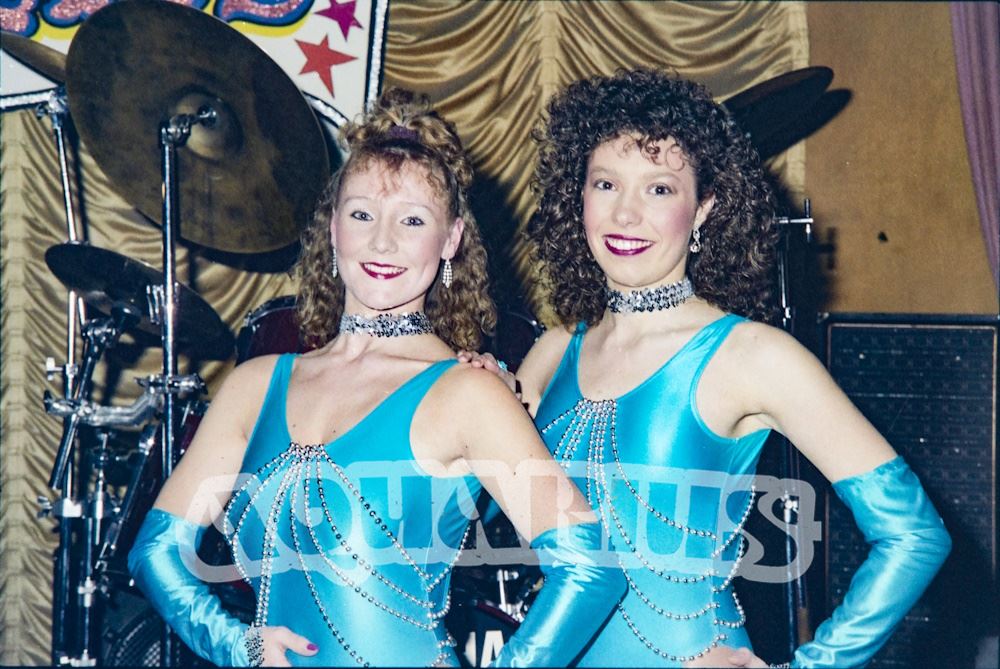 Two dancers in leotards on stage in front of the resident band