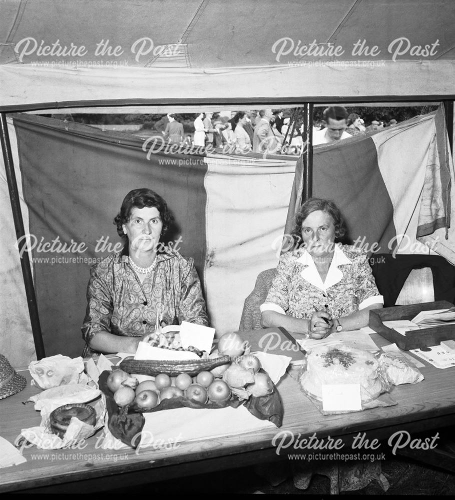 Two ladies with a display of fruit, pork pie and cake at a Stanton Works Annual Flower Show