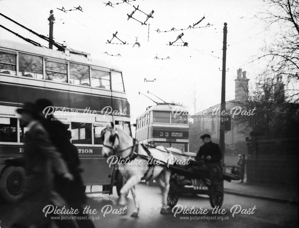 Traffic congestion, horse and cart, trolley buses and workers crowd the street on Osmaston Road