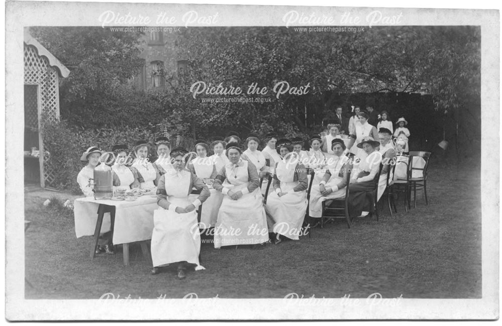 Group of women and nurses seated at a table in the grounds of a house