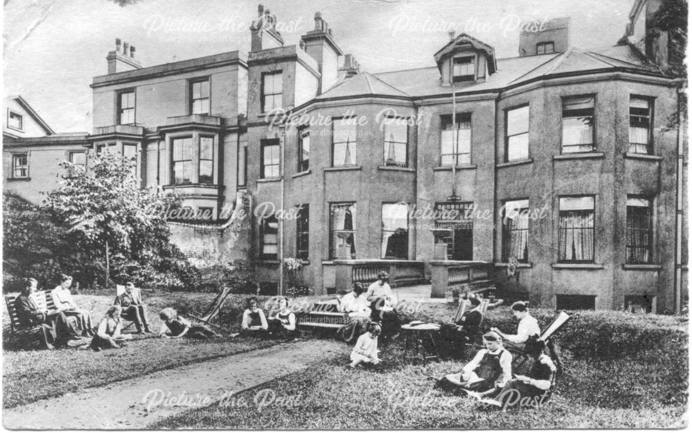 Back garden of a large house (school?) on a built-up street with young women reading