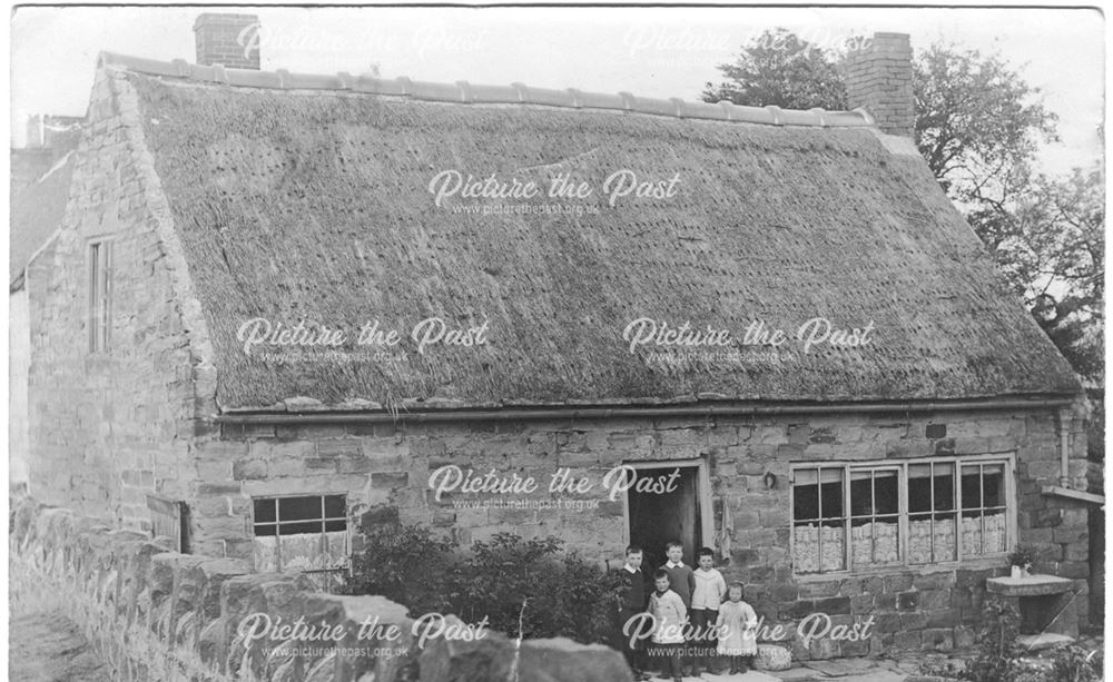 thatched house with family group of children standing in the doorway