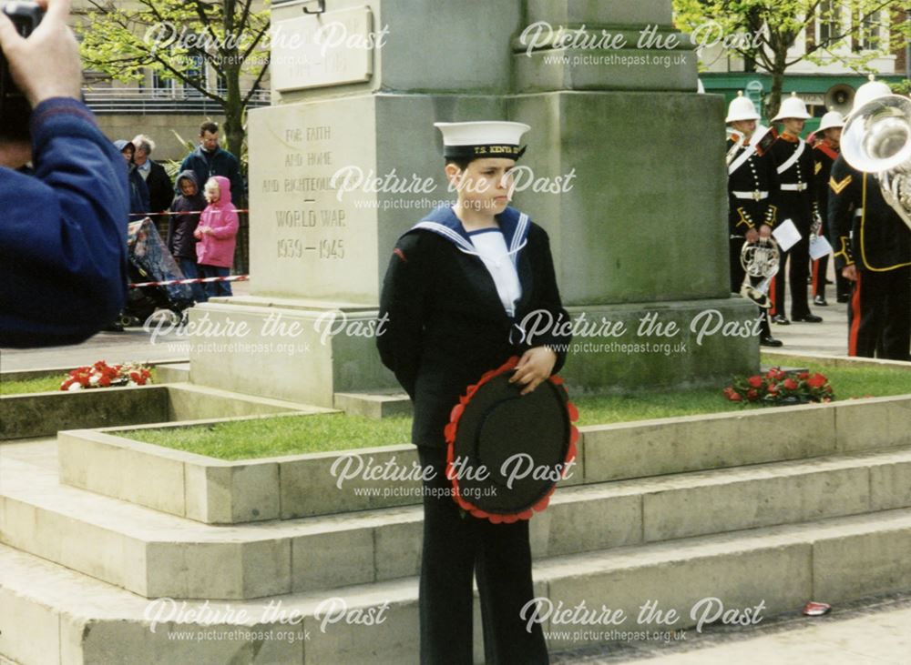 A naval cadet holding a wreath by the war memorial during a Royal Navy and Royal Marines visit to De